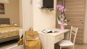 A hotel room with a bed, a desk with a chair, a television, and a pink flower vase. - Marilu B&B (Matino)