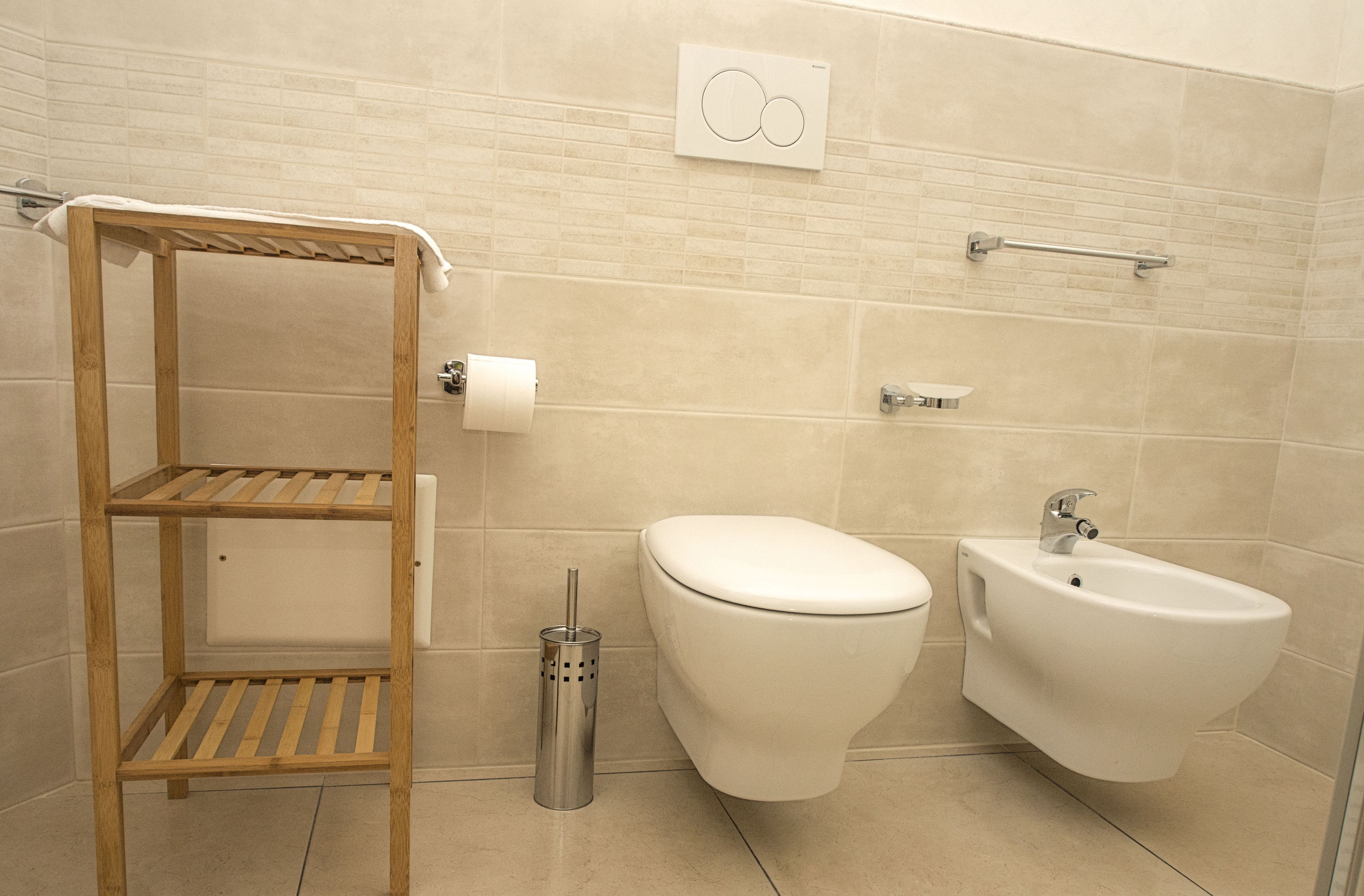 Une salle de bain moderne équipée de toilettes, d’un bidet et d’une étagère en bois.