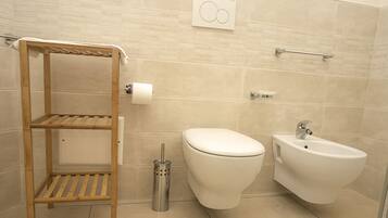 Une salle de bain moderne équipée de toilettes, d’un bidet et d’une étagère en bois.