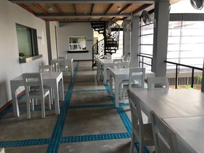 A dining area with white tables and chairs, a blue-tiled floor, and a staircase in the background. - Beach Paradise by Oceanfront Condos (Nilaveli)