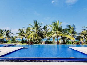A clear blue pool surrounded by palm trees and a view of the ocean. - Beach Paradise by Oceanfront Condos (Nilaveli)
