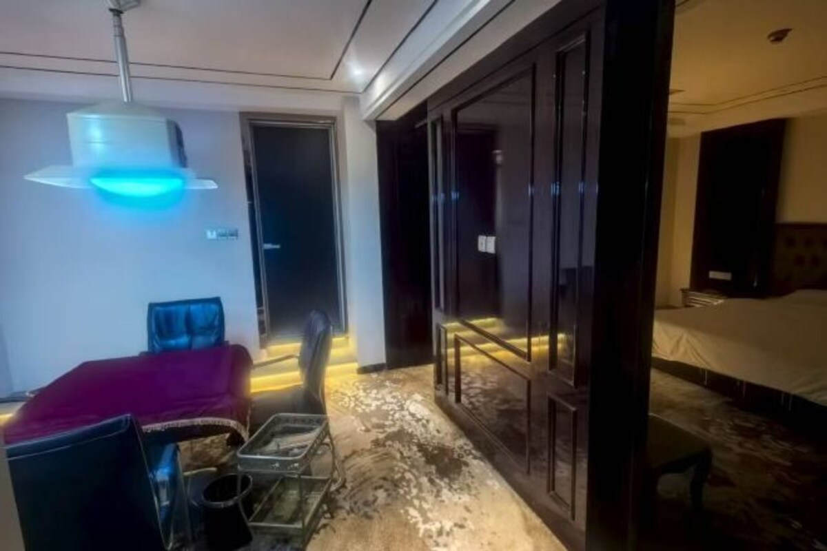 A hotel room with a bed, a desk, and a chair. There is a door leading to another room and a window with curtains.