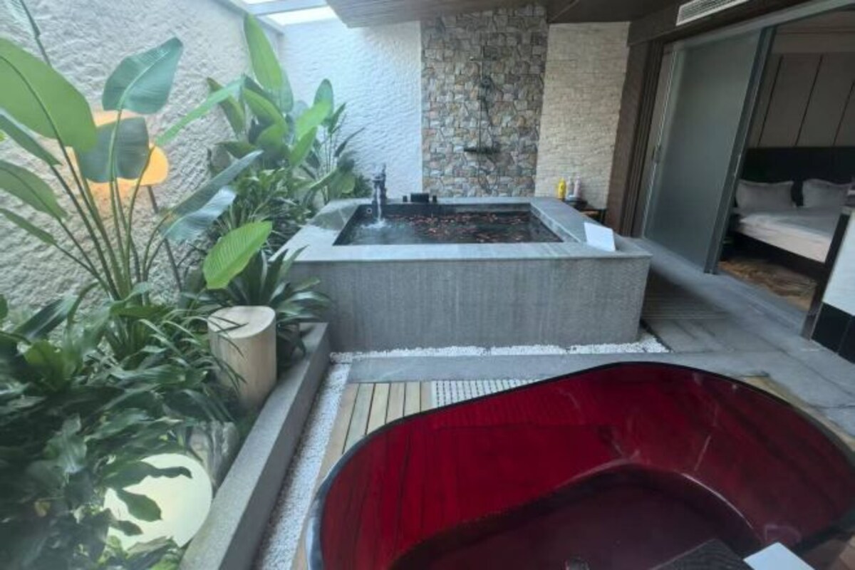 A spa area with a rectangular hot tub and a red hot tub, surrounded by potted plants and a stone wall.