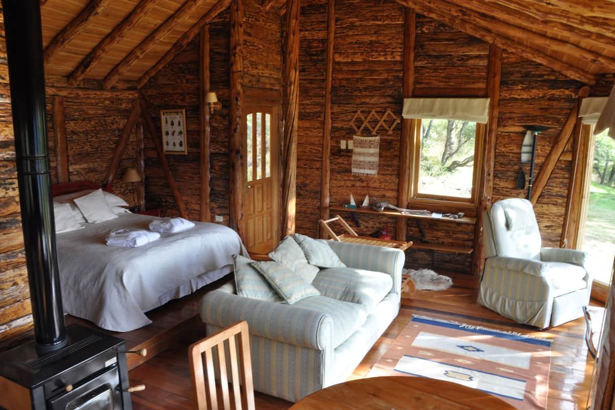 Un chalet confortable avec un lit, un canapé et un fauteuil, des murs en bois et une grande fenêtre.