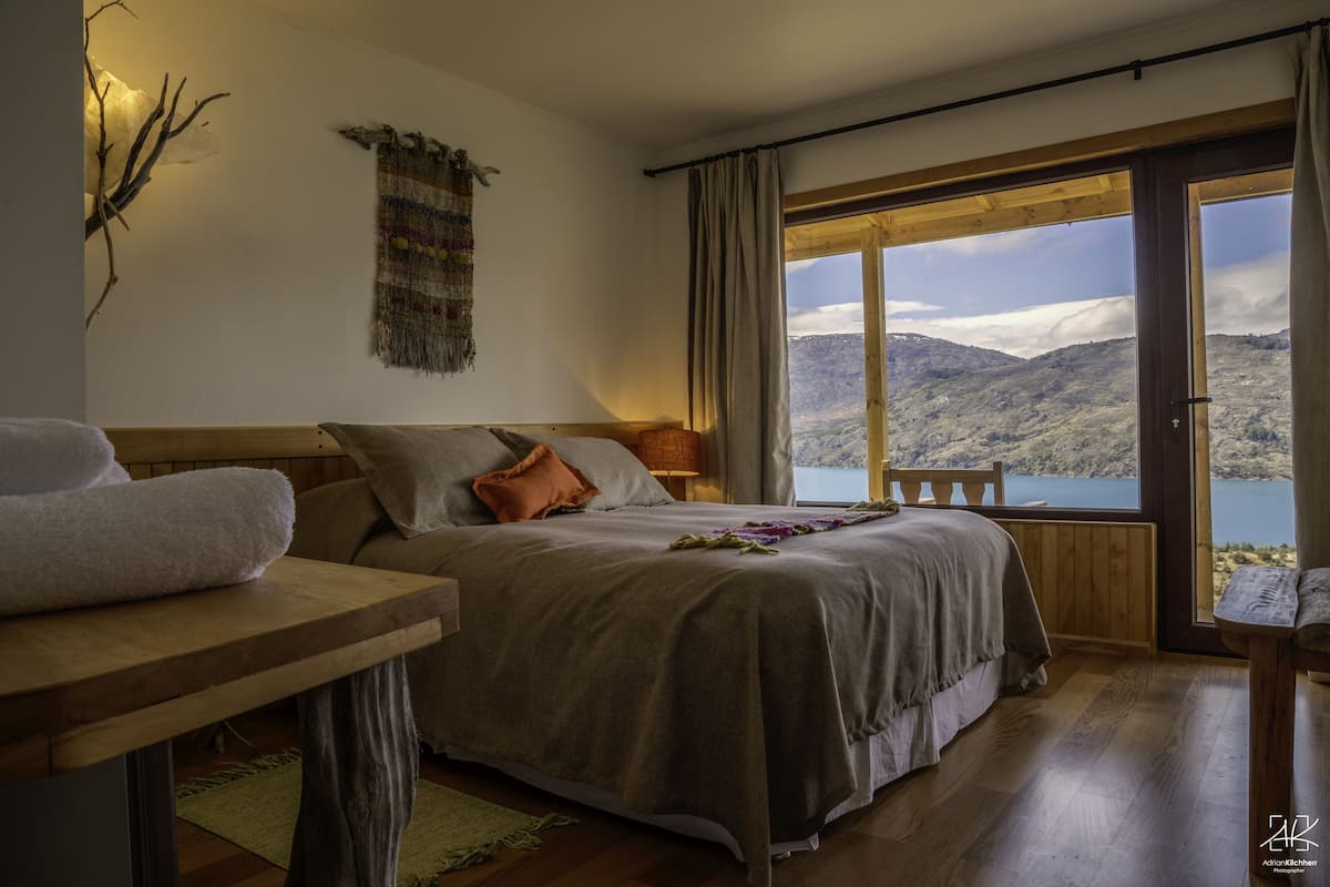 Une chambre avec un grand lit, une table en bois et une vue sur un lac et des montagnes.
