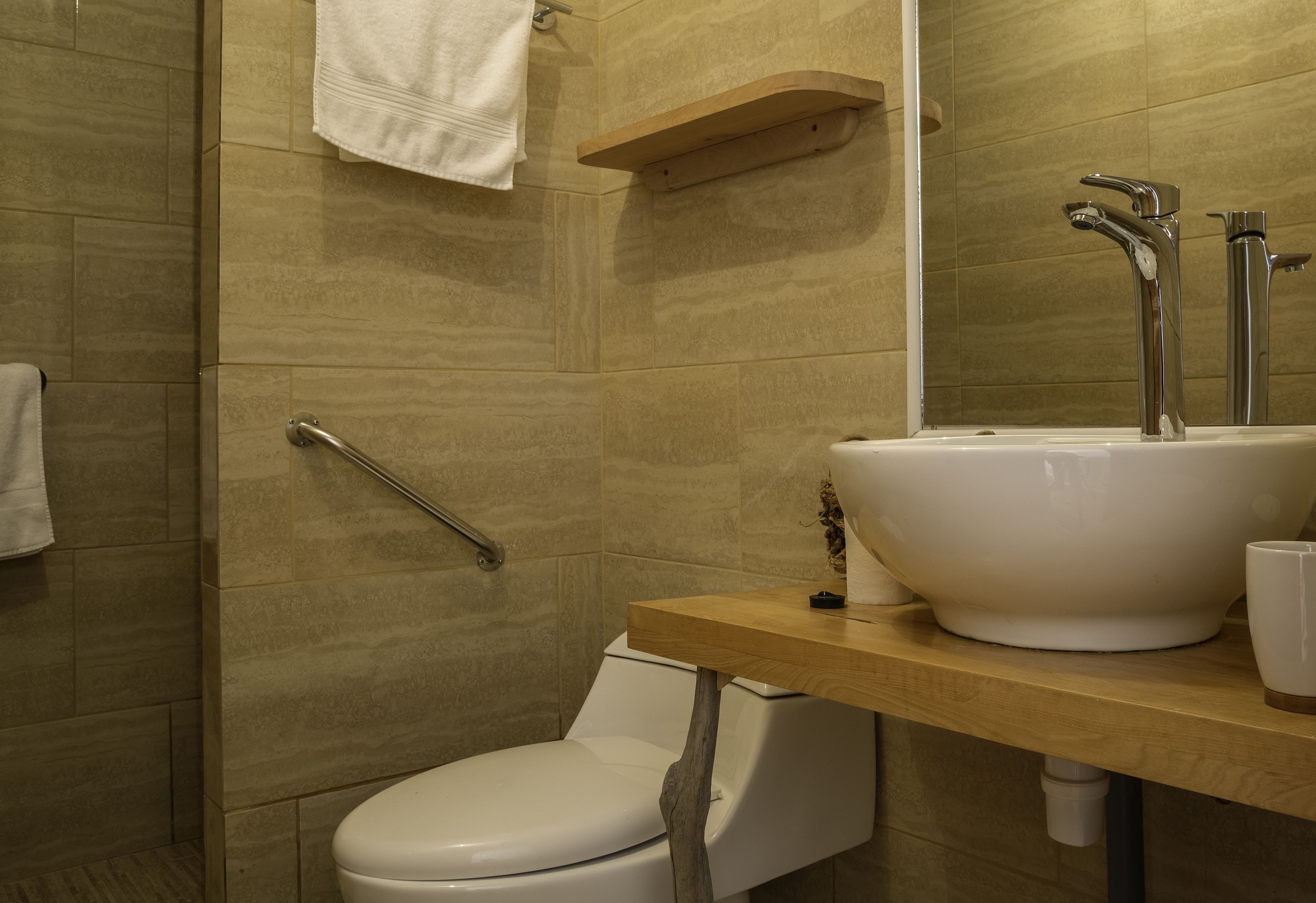Une salle de bain avec des toilettes blanches, un lavabo surmonté d’un miroir et une serviette accrochée au mur.