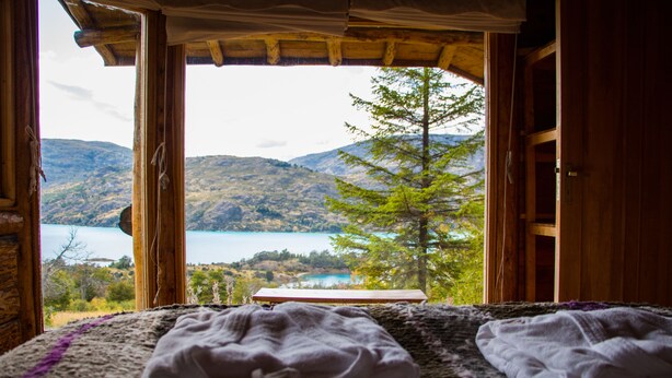 Een kamer met een bed, uitzicht op een meer en bergen op de achtergrond.