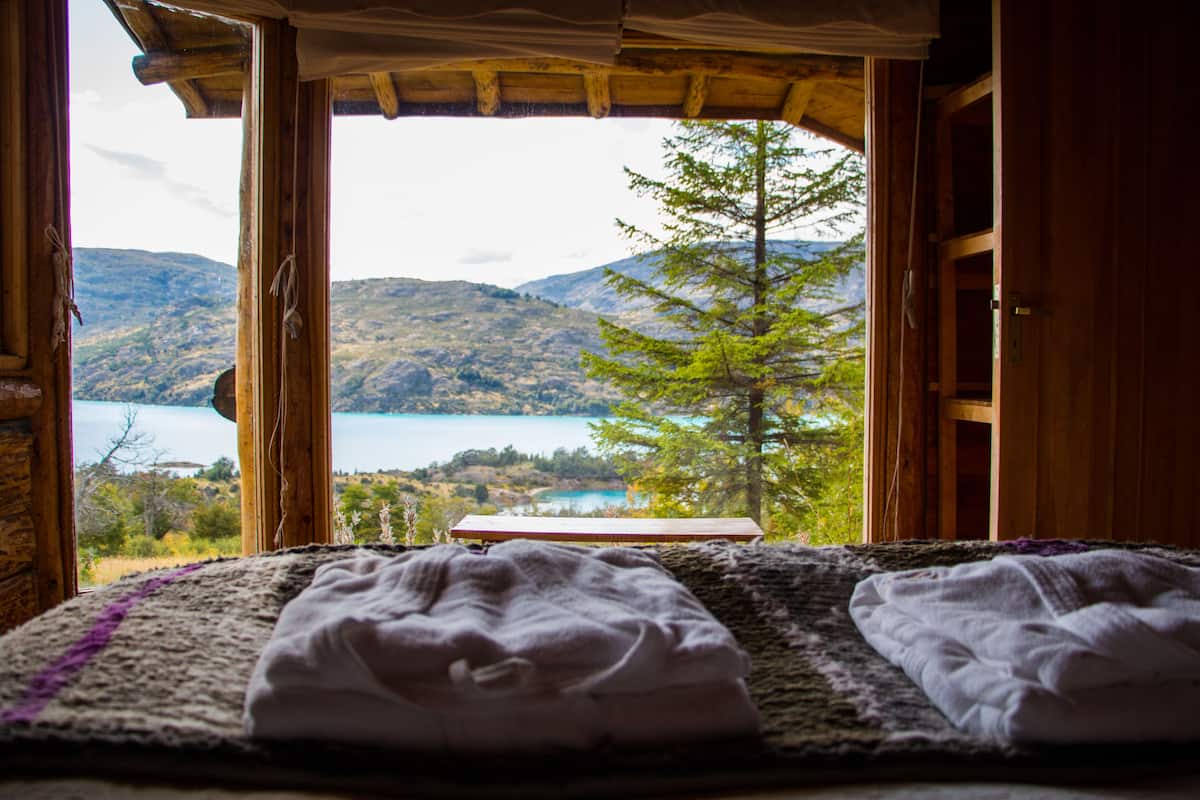 Une chambre avec un lit, donnant sur un lac, et avec des montagnes en arrière-plan.
