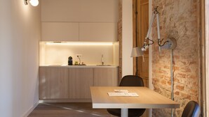 A narrow hallway with a wooden ceiling, a kitchen area with a white countertop and modern appliances, and a dining area with a table and chairs. - San Lorenzo Suites (San Lorenzo de El Escorial)