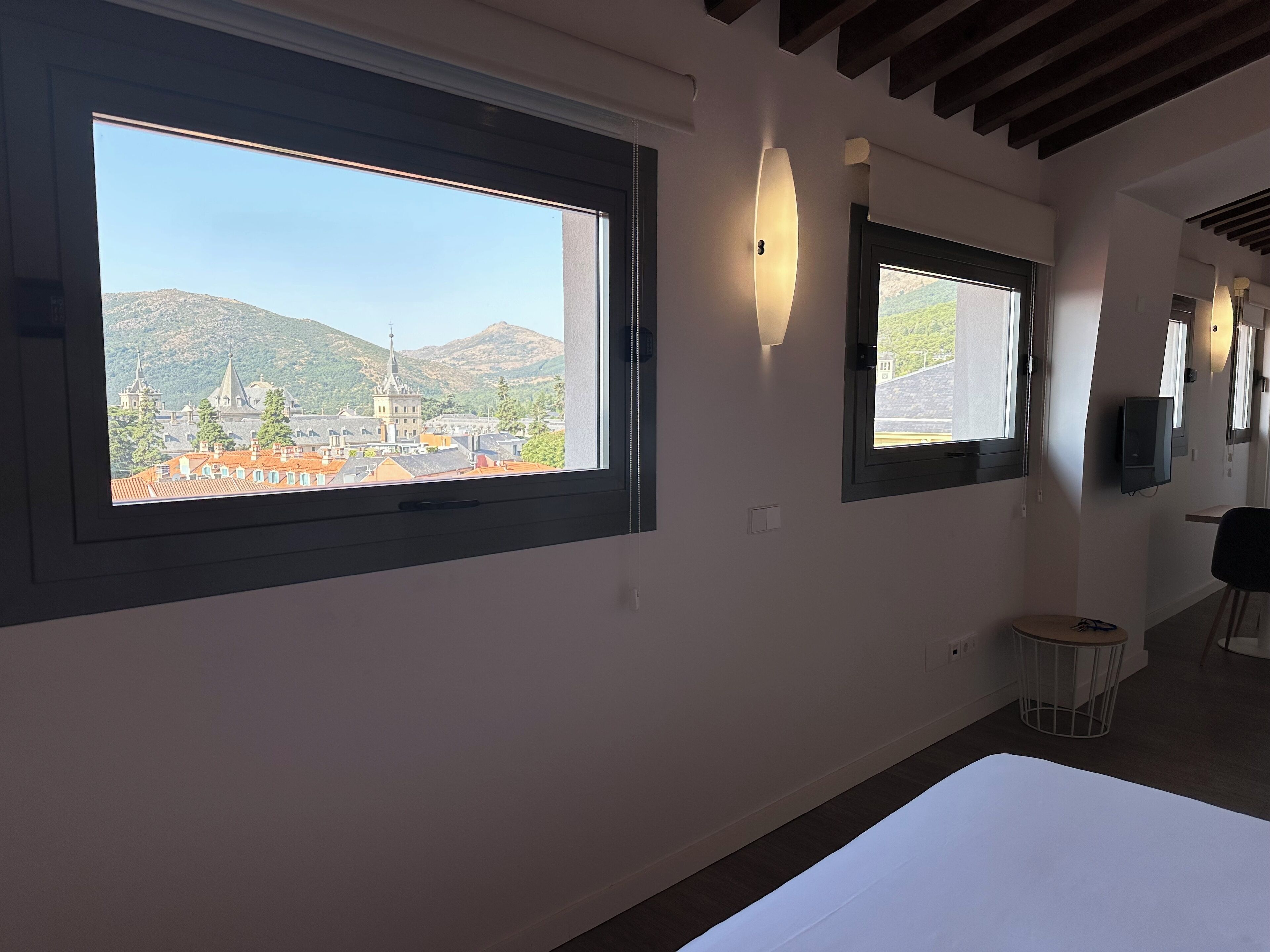 A modern hotel room with large windows offering a view of a historic town and mountains.