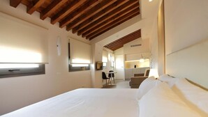 A hotel room with a large bed, a desk, and a kitchenette in the background. - San Lorenzo Suites (San Lorenzo de El Escorial)