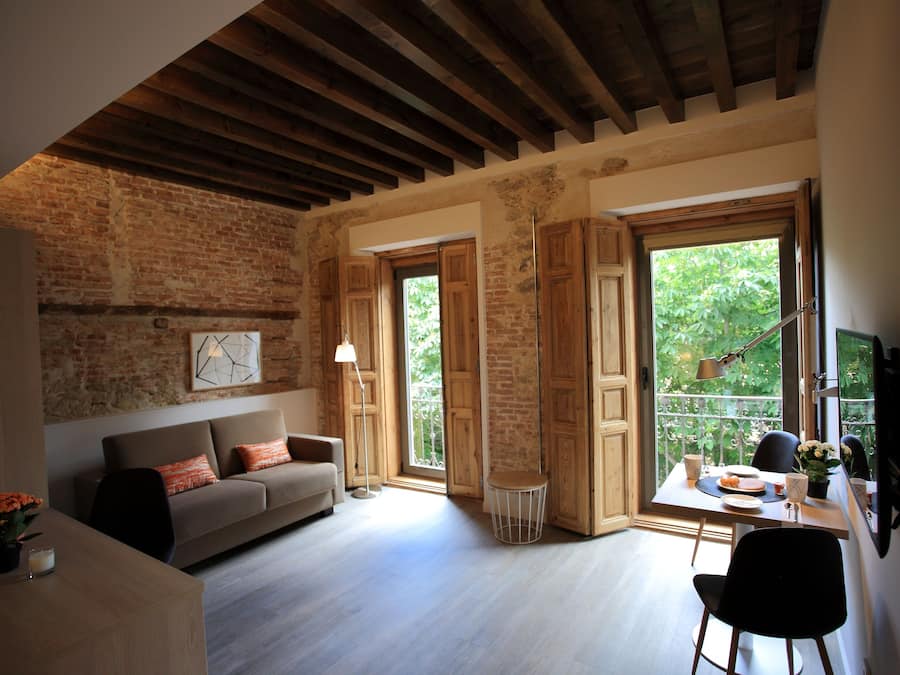 Una sala de estar acogedora con un sofá, una mesa de comedor y un televisor. Se ve un ventanal con vistas a zonas verdes.