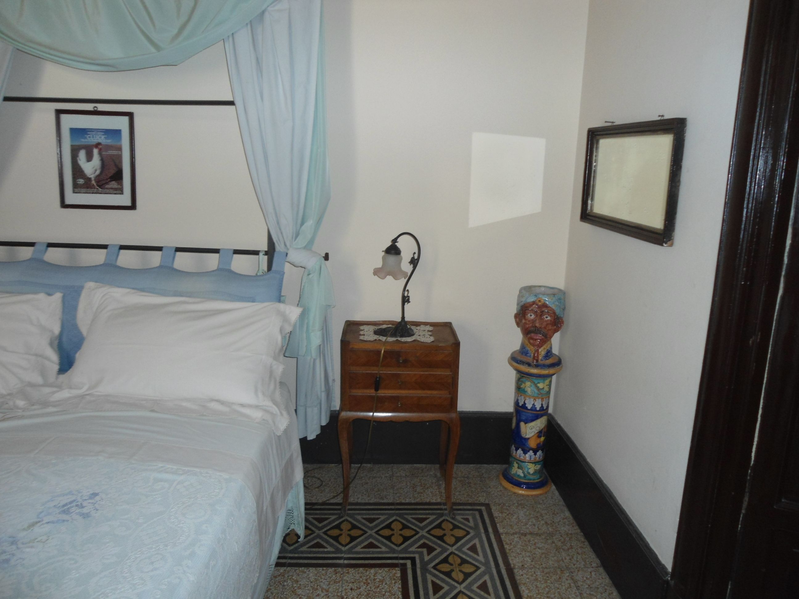 A bedroom with a bed, a nightstand, a decorative vase, and a framed picture on the wall.