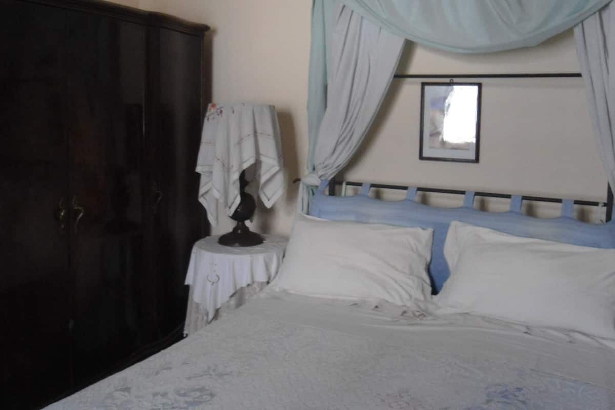 Quarto com cama, mesa de cabeceira, guarda-roupa e janela com cortinas.