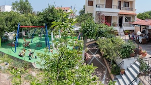 Zona residencial con un parque infantil, una escalera que lleva a un balcón y un patio con mobiliario exterior.
