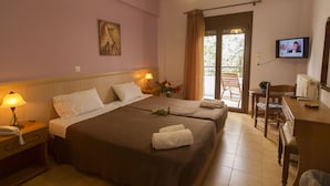 Habitación de hotel con dos camas, un escritorio, televisor y balcón con vistas.