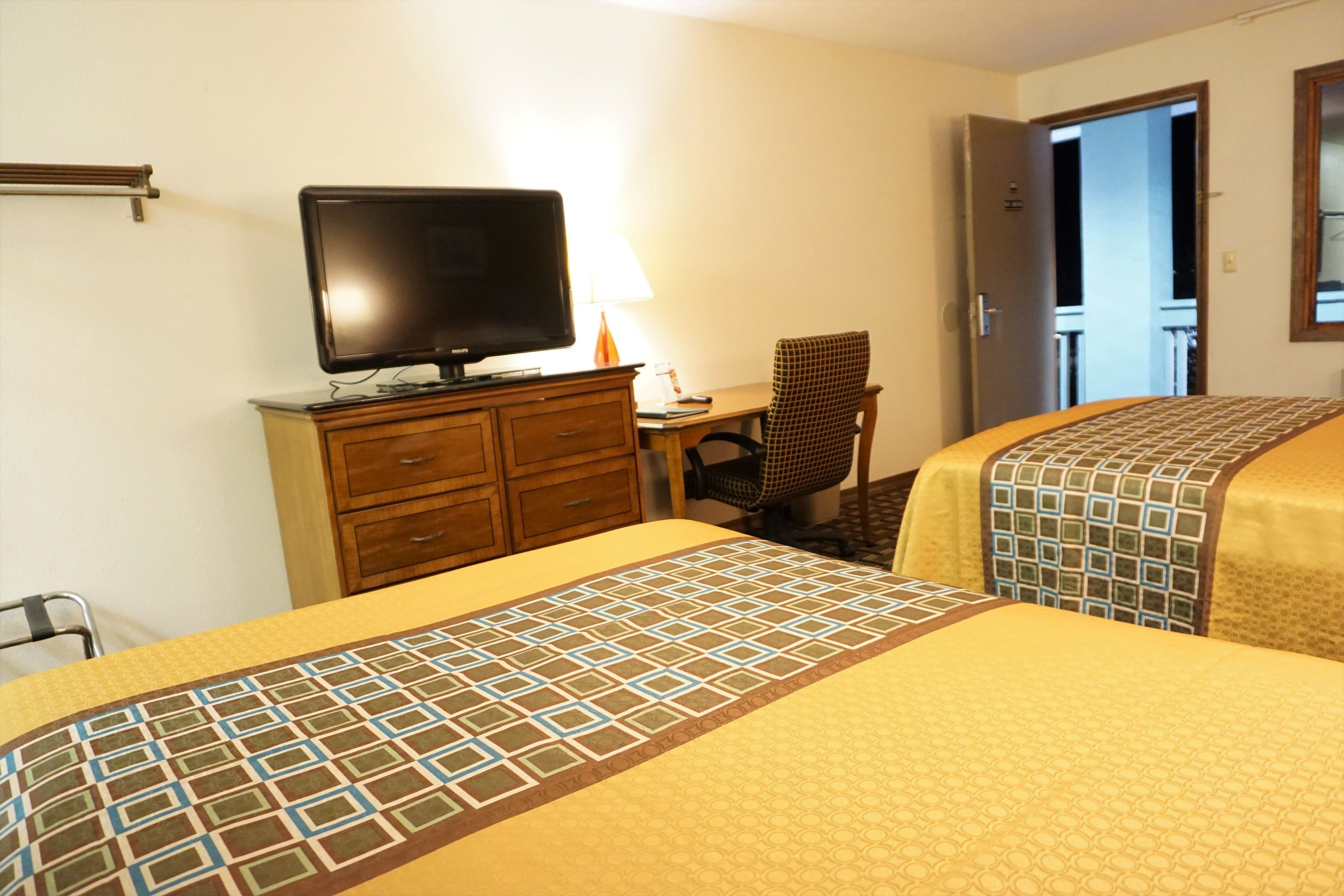 A hotel room with two beds, a desk with a computer, a chair, and a television.