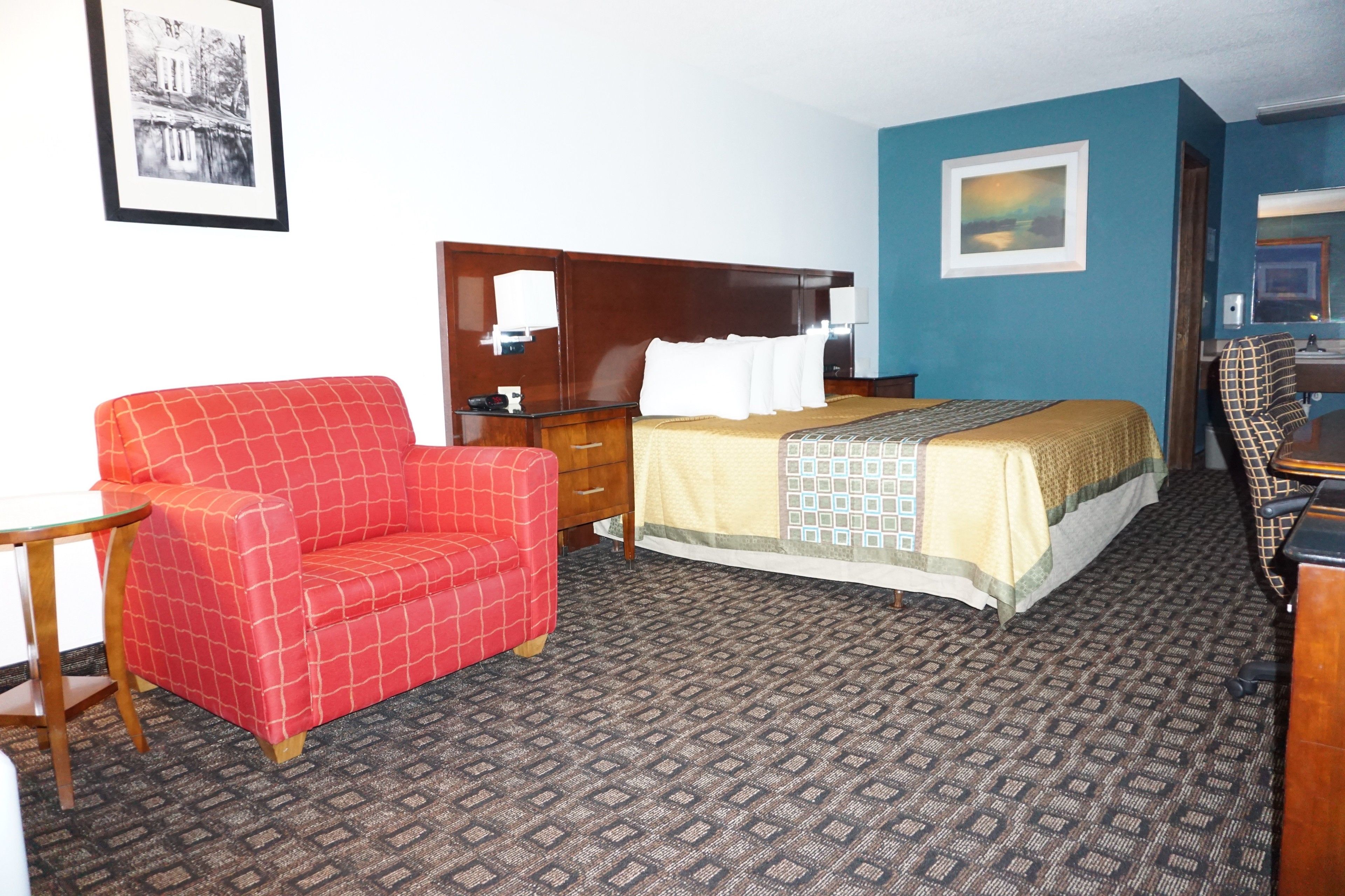 A hotel room with a bed, a red sofa, a wooden nightstand, a desk, and a mirror.