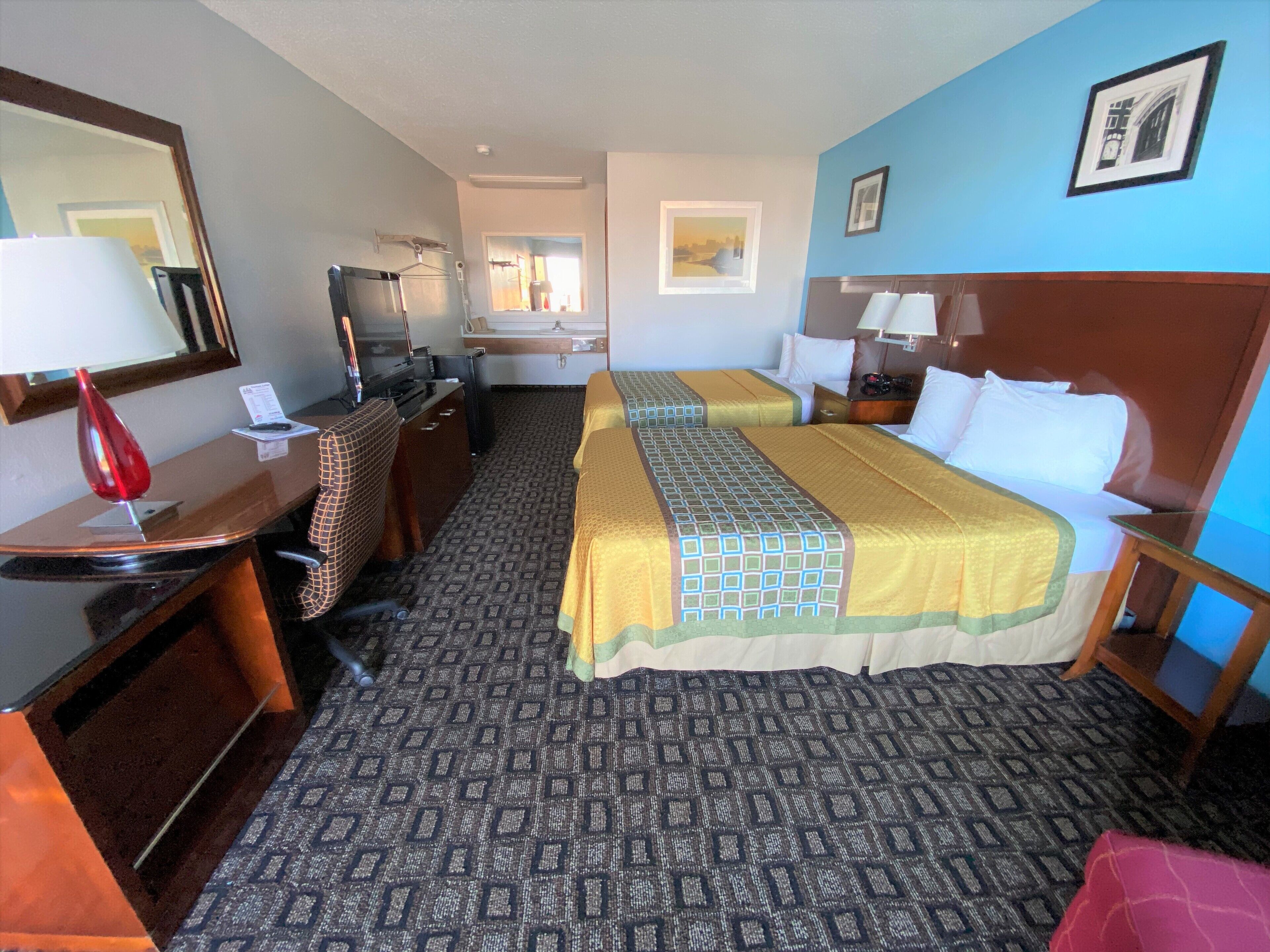 Een hotelkamer met twee bedden, een bureau, een stoel, een televisie en een spiegel.