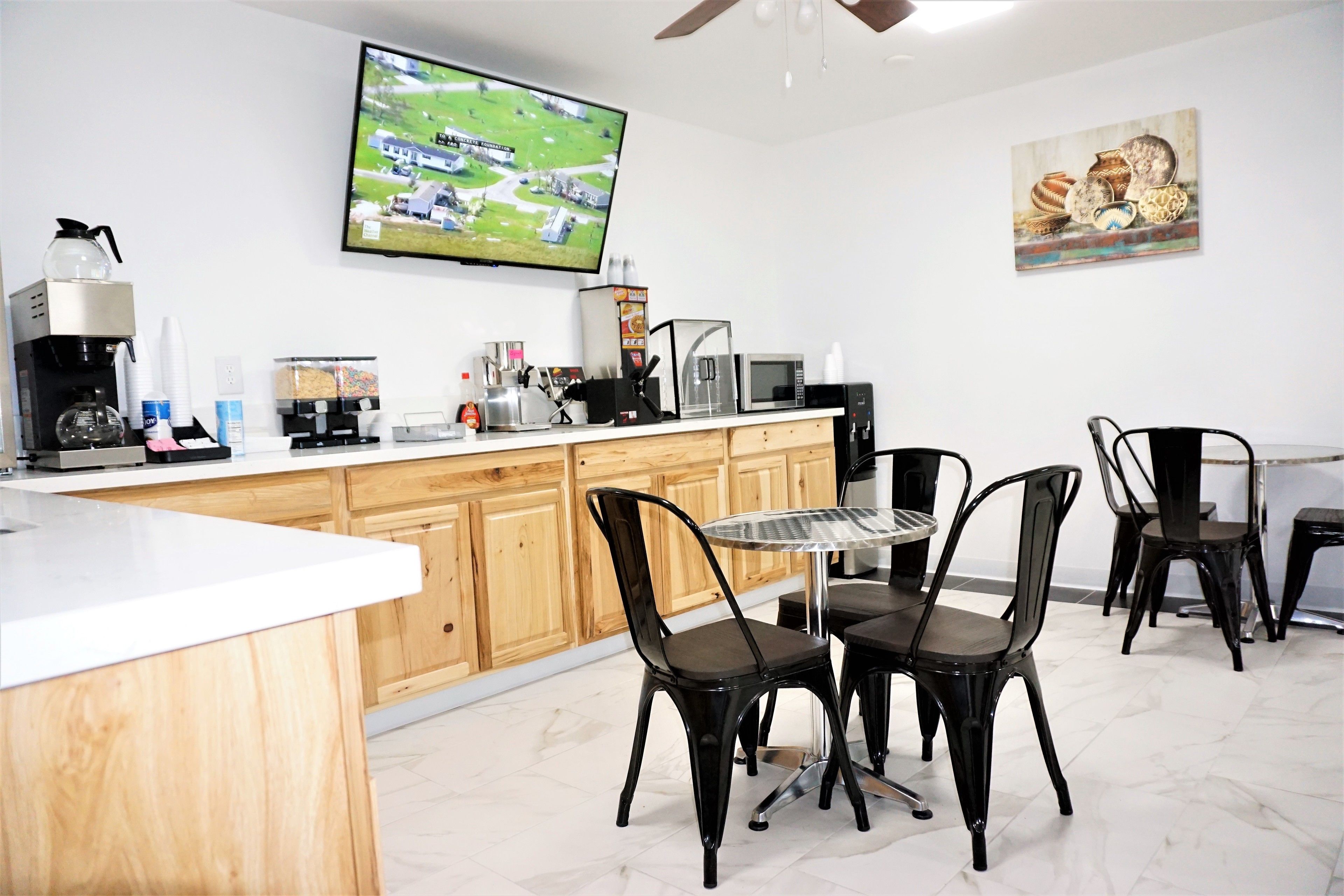 A modern kitchen with a dining area, featuring a TV, coffee maker, microwave, and wooden cabinets.