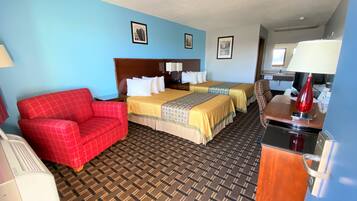 A hotel room with two beds, a red armchair, a desk with a lamp, and a patterned carpet.