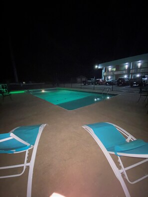 Une piscine la nuit, avec deux chaises longues et un bâtiment en arrière-plan.