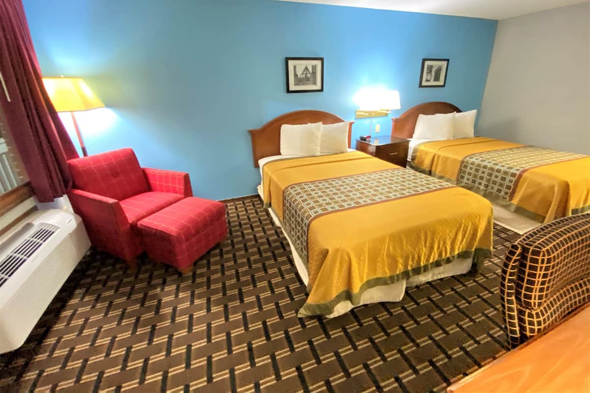 Una habitación de hotel con dos camas, un sillón rojo, un calentador y dos lámparas de pared.