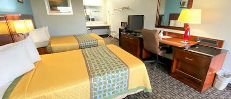 A hotel room with two beds, a desk, a chair, a TV, a mirror, and a lamp.