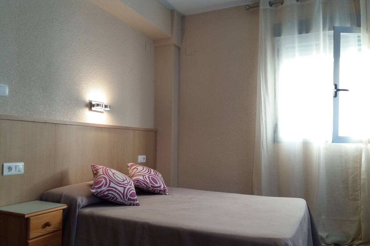 Une chambre à coucher avec un lit, deux oreillers, une table de chevet et une lampe fixée au mur.