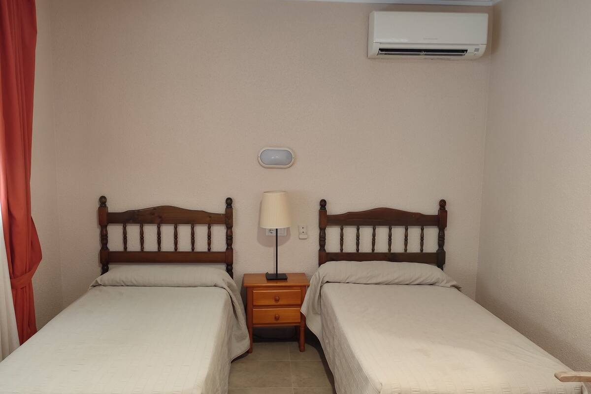Une chambre double avec deux lits, une table de chevet, une lampe et un appareil de climatisation.