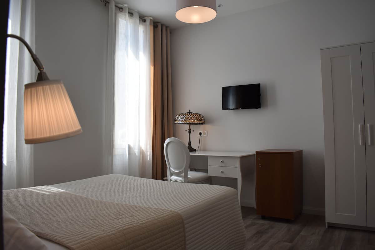 Ein Hotelzimmer mit Bett, Schreibtisch, Stuhl, Fernseher und Kleiderschrank.