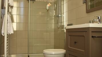 Une salle de bain avec une douche à parois de verre, des toilettes blanches, un meuble-lavabo avec un miroir et un tapis rouge sur le sol.