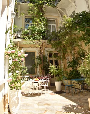 A courtyard with a table and chairs, surrounded by potted plants and a balcony. - Hotel Henri IV (Tarbes)