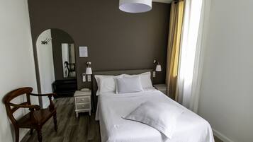 A hotel room with a bed, a wooden chair, a nightstand, a lamp, and a mirror.