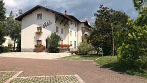 A building with the name 'Gilda' on the facade, featuring a paved entrance, a small garden with flowers, and a brick pathway leading to the entrance. - Albergo Gilda (Caldonazzo)
