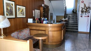 A reception area with a wooden counter, a bench, a small table, and a staircase leading upstairs. - Albergo Gilda (Caldonazzo)