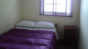 Un dormitorio pequeño y sencillo con cama, mesita de noche y ventana con persianas.