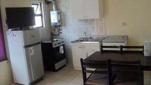 Una cocina pequeña con refrigerador, estufa, horno, lavamanos y una mesa de comedor con sillas.