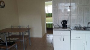 Cocina con armarios blancos, una encimera y un hervidor. Hay una mesa de comedor con sillas.