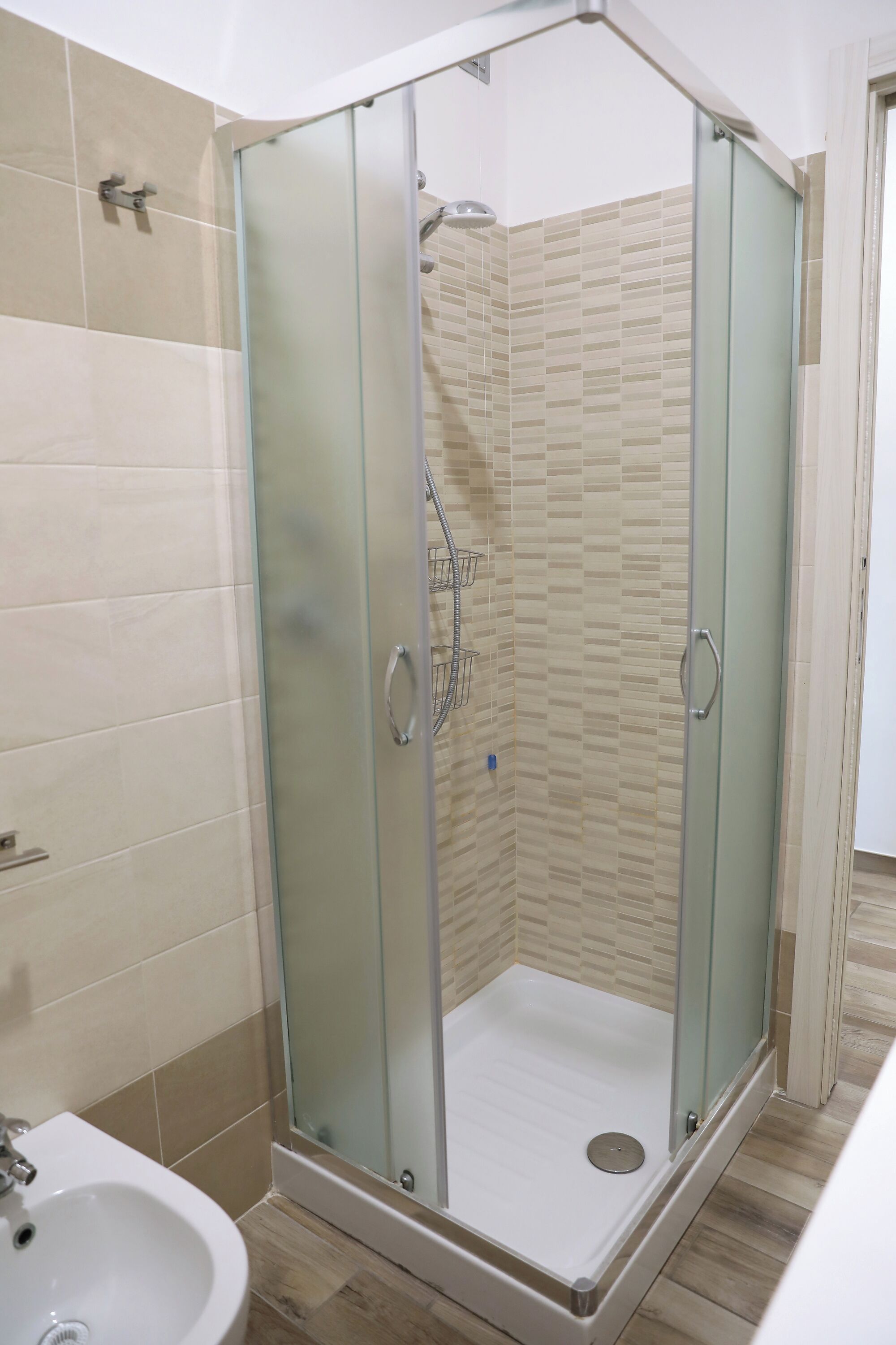 Un box de ducha con paredes de vidrio, un revestimiento de azulejos y un lavamanos blanco a la izquierda.