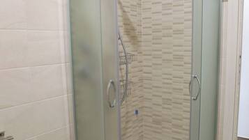Un box de ducha con paredes de vidrio, un revestimiento de azulejos y un lavamanos blanco a la izquierda.