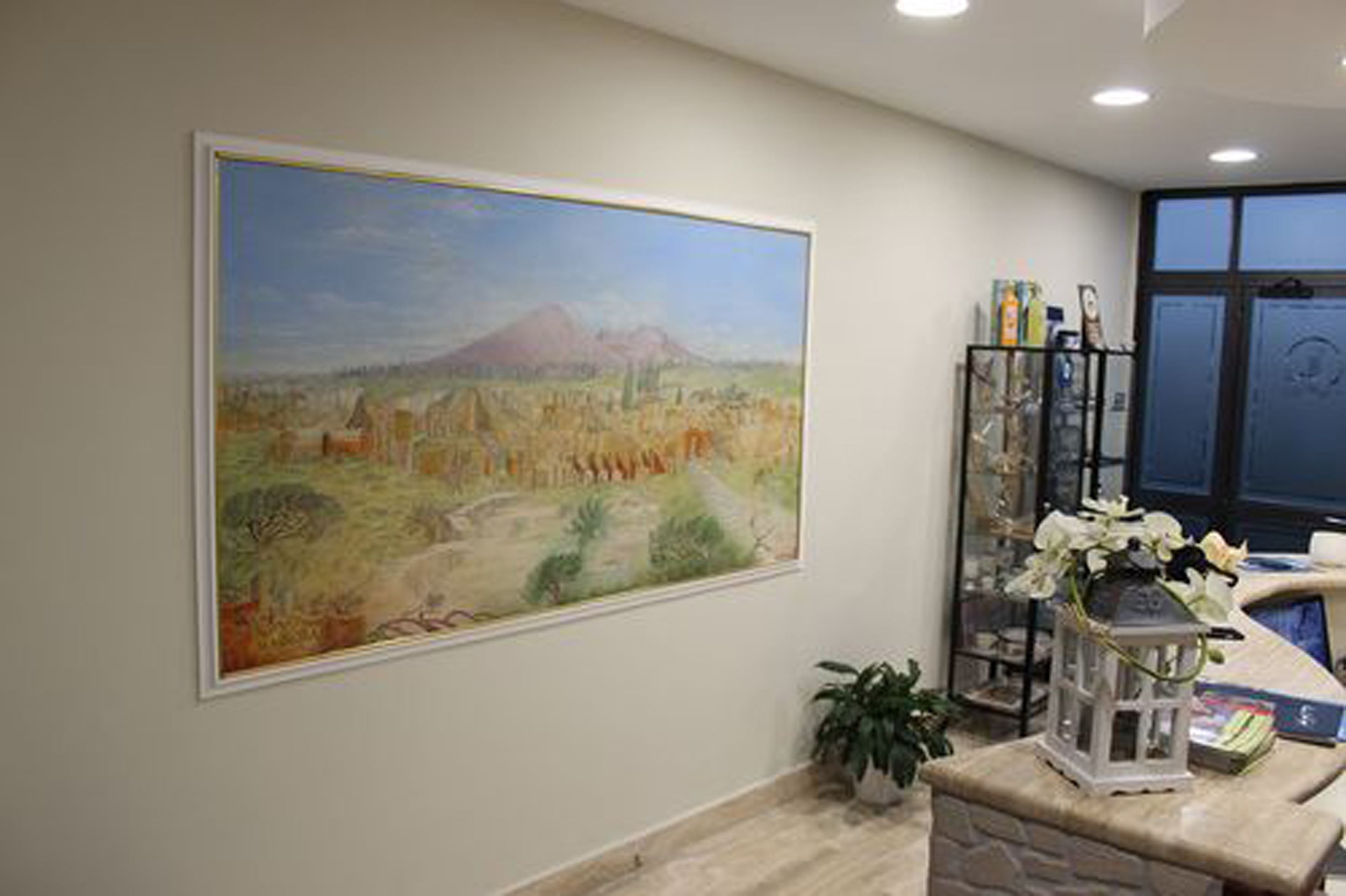 Pintura de uma paisagem com uma montanha, uma receção com um vaso de flores e uma planta no chão.