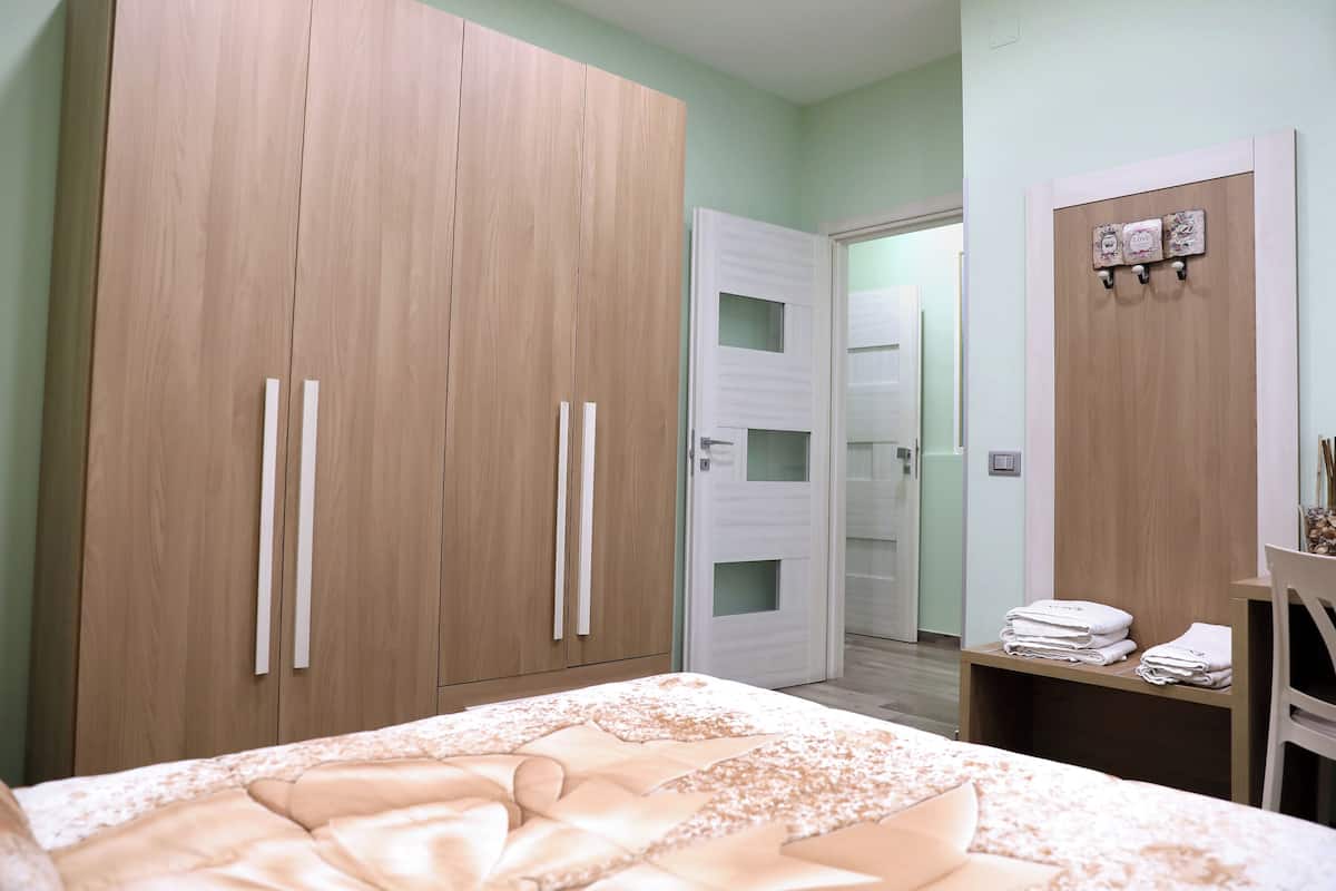 A bedroom with a large wardrobe, a bed with a floral duvet, and a small table with towels.
