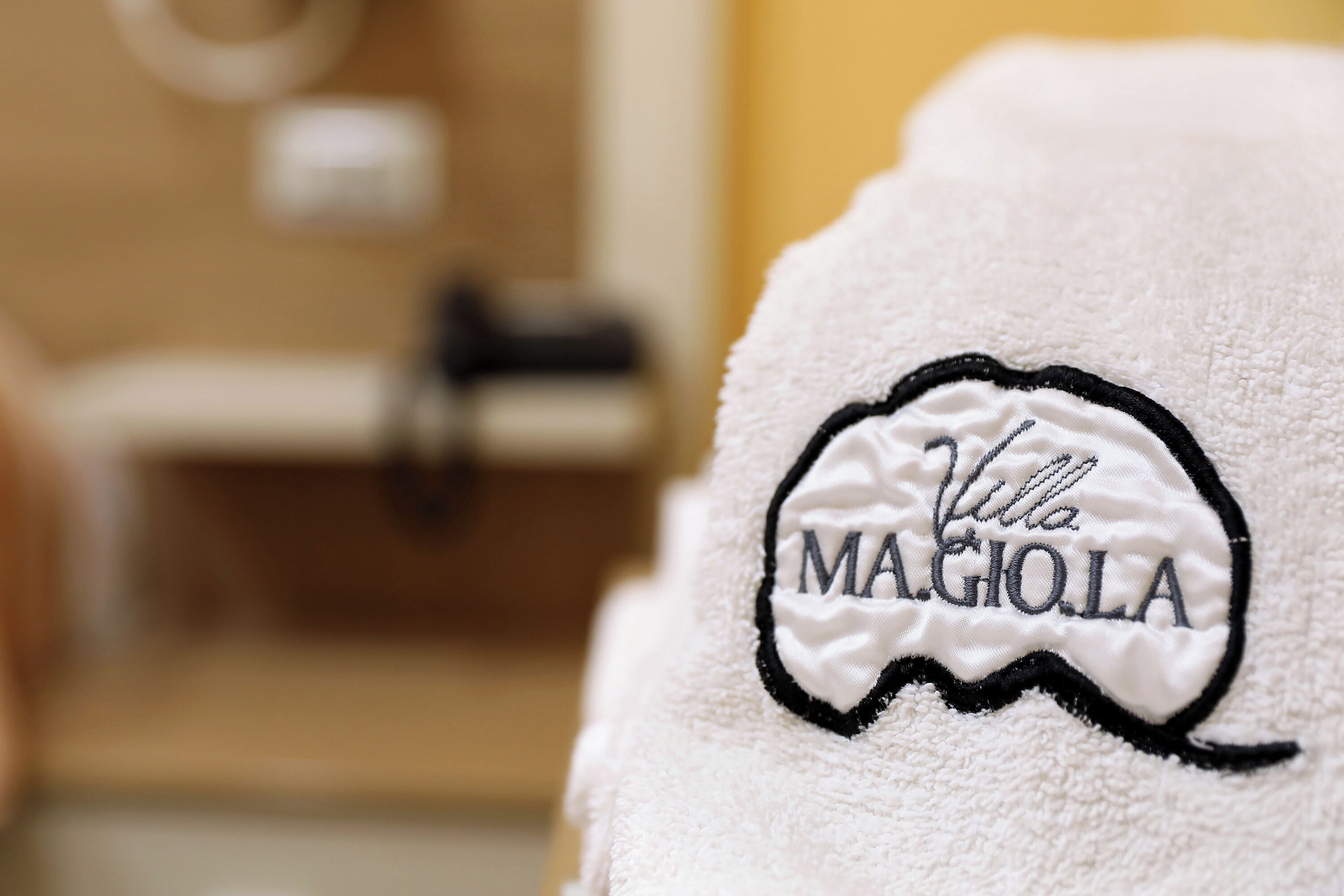 A white towel with embroidered text "Villa Magiola" in a bathroom setting.