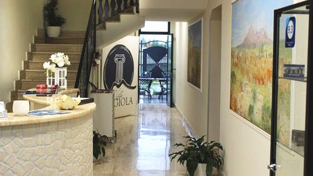 A hotel lobby with a reception desk, a staircase, and a mural on the wall. - Villa Magiola (Pompei)