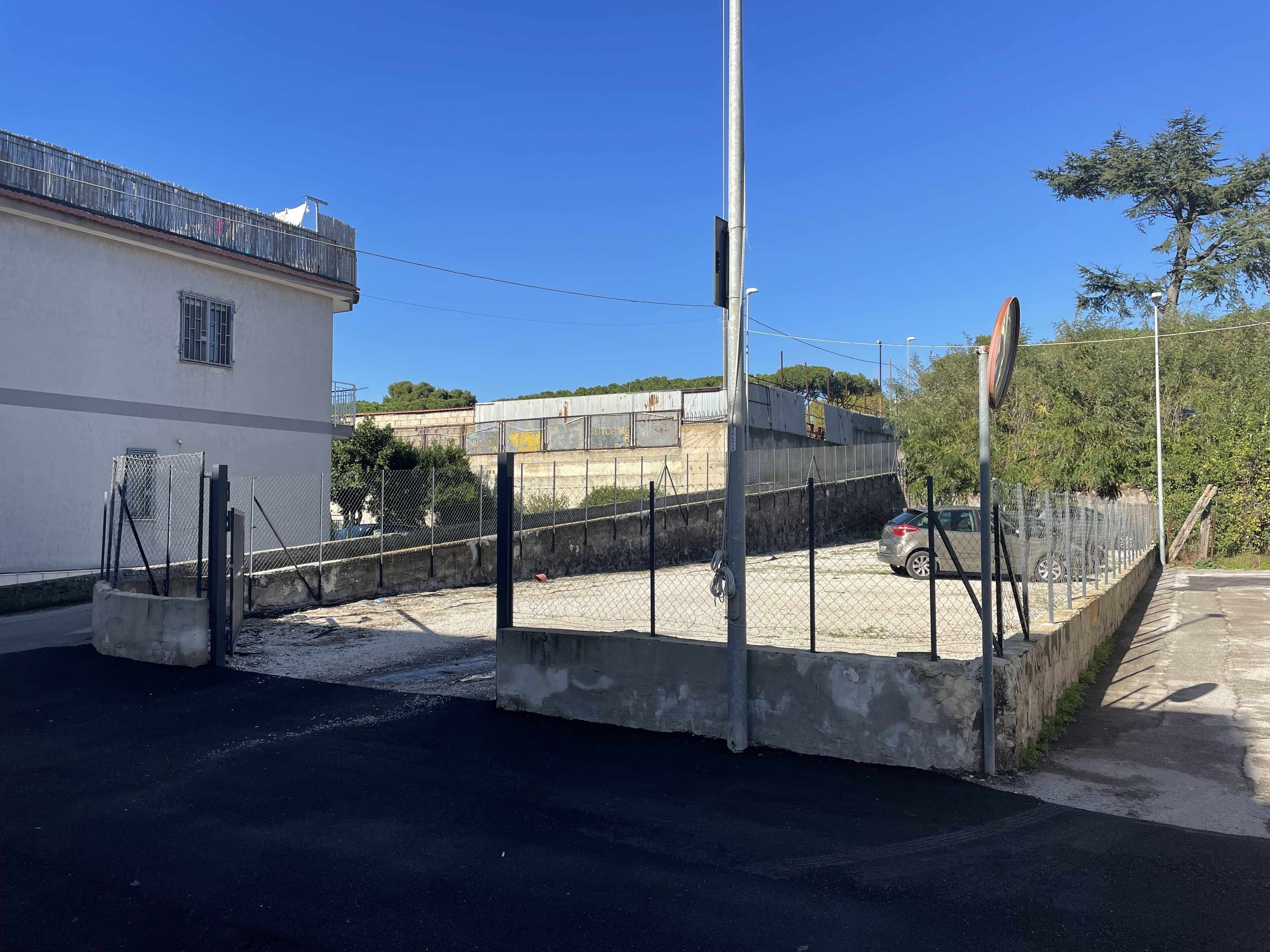 Un espace de stationnement clos, doté d’une barrière en béton, d’une clôture métallique et d’un lampadaire.
