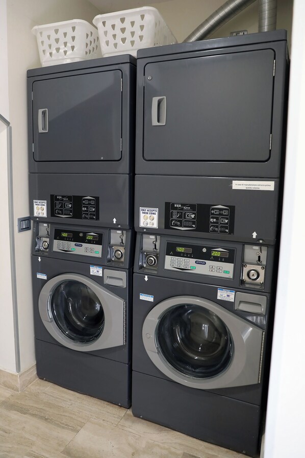 A pair of stacked front-loading washing machines with control panels and a small window on the top unit.