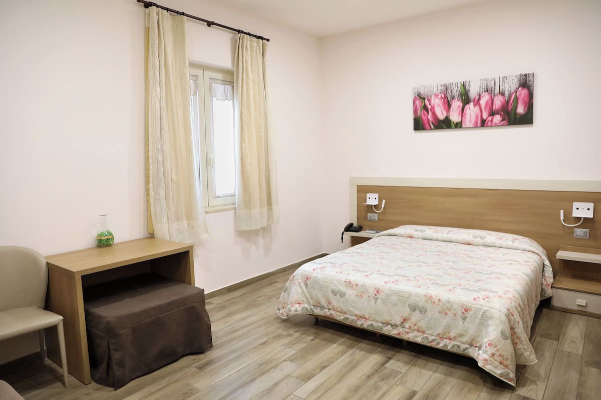 A bedroom with a bed, a desk, a chair, and a window with curtains.