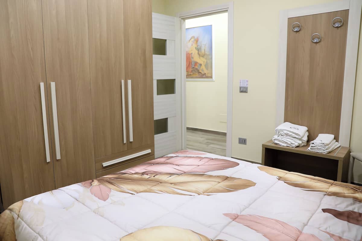A bedroom with a bed, wooden wardrobe, and a small table with towels.