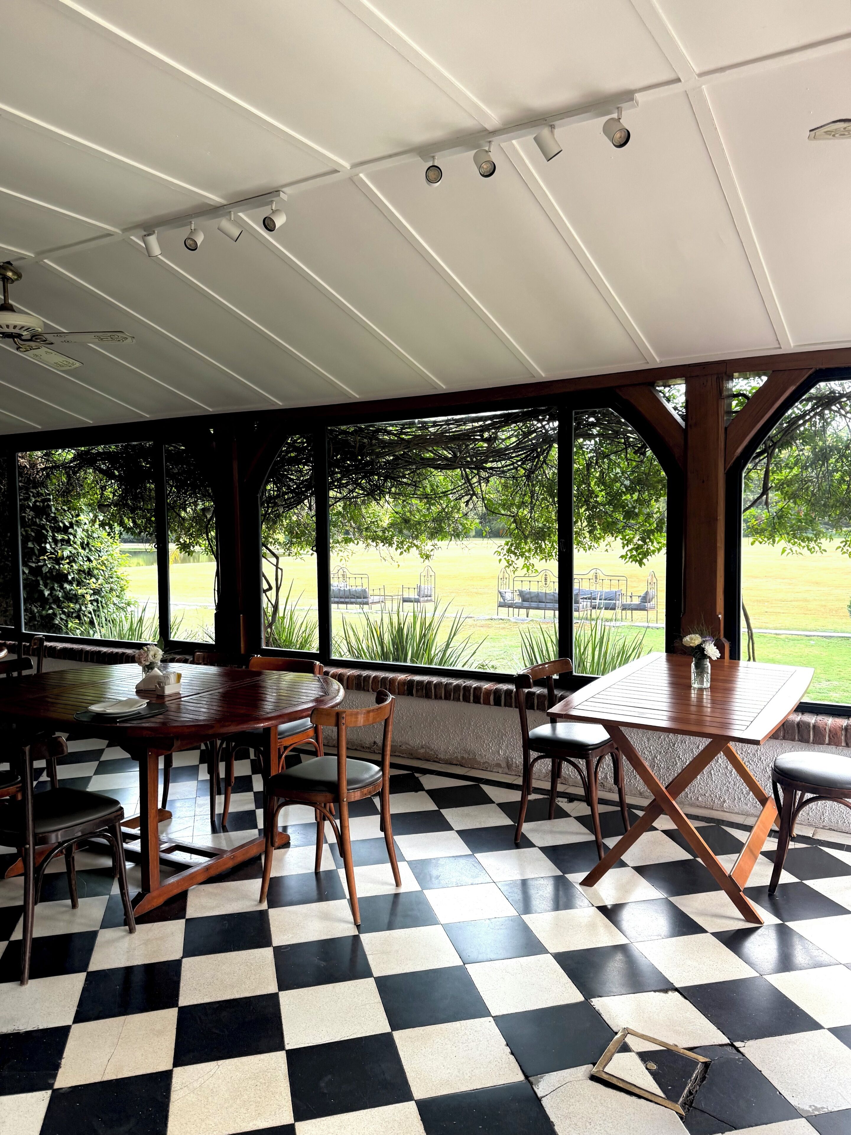 A covered outdoor seating area with checkered flooring, wooden tables, and chairs.